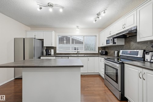 Kitchen featuring wood-finish flooring, white cabinetry, dark countertops, a large window, and track lighting - 1804 121 Street, Edmonton, AB 