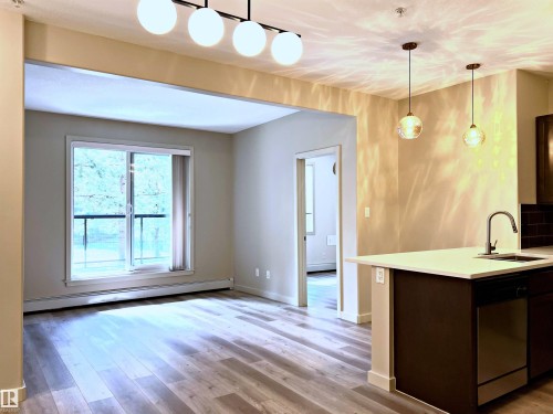 Open-concept living area featuring wood-finish flooring, a sliding glass door to a balcony, and a modern linear chandelier - 140 308 Ambleside Link Link, Edmonton, AB 