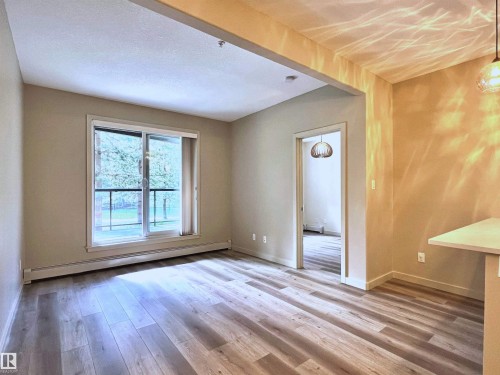 Living area with wood-finish flooring, neutral wall tones, and a sliding glass door providing external access - 140 308 Ambleside Link Link, Edmonton, AB 