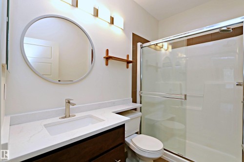 Bathroom featuring a dark wood-finish vanity with an integrated white sink, a white countertop, and a circular mirror - 140 308 Ambleside Link Link, Edmonton, AB 
