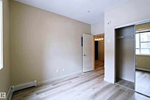 Bedroom featuring wood-finish flooring, neutral wall tones, and a closet with mirrored sliding doors - 140 308 Ambleside Link Link, Edmonton, AB 