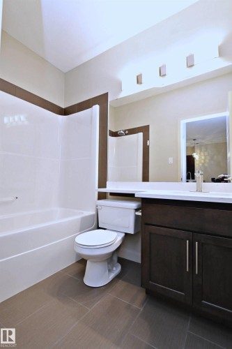 Bathroom featuring a white bathtub with a shower, a dark wood-finish vanity with a light countertop, and tile flooring - 140 308 Ambleside Link Link, Edmonton, AB 