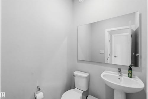 Pedestal sink with chrome faucet, white toilet, and a large wall-mounted mirror - 33 1729 Keene Crescent, Edmonton, AB 