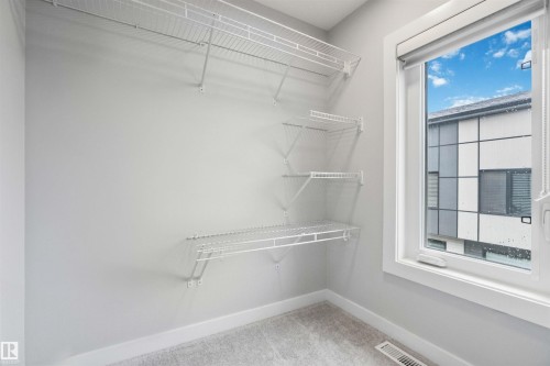 Storage area featuring white wire shelving units, a white-framed window, light gray walls, and gray carpet flooring - 33 1729 Keene Crescent, Edmonton, AB 