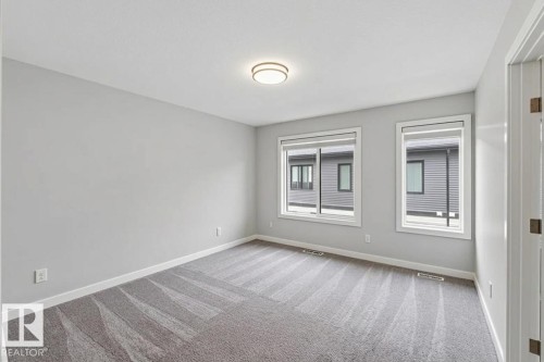 Spacious interior room with light grey walls, patterned carpeting, and white trim - 33 1729 Keene Crescent, Edmonton, AB 