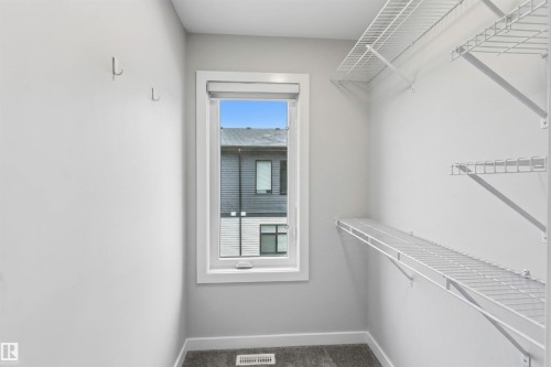 Walk-in closet featuring wire shelving, wall-mounted hooks, white trim, and a window - 33 1729 Keene Crescent, Edmonton, AB 