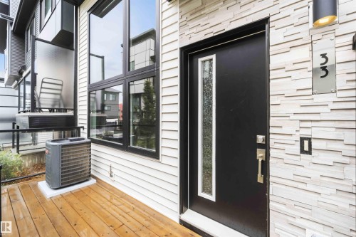 Modern exterior featuring a black entry door with a vertical frosted glass insert, stone veneer siding, and a wood-finish deck - 33 1729 Keene Crescent, Edmonton, AB 