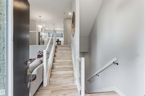 Foyer featuring a contemporary glass and wood railing staircase, wood-finish flooring, recessed lighting, and a dark entry door - 33 1729 Keene Crescent, Edmonton, AB 