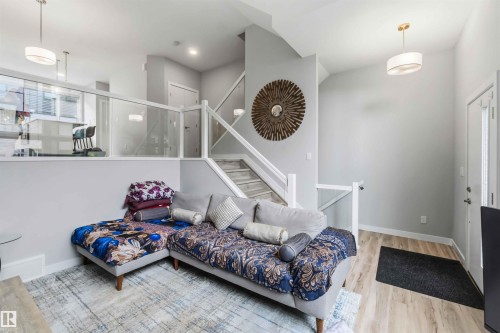 Open-concept living space featuring light wood-finish flooring, a contemporary staircase with glass railing, and a modern pendant light fixture - 33 1729 Keene Crescent, Edmonton, AB 