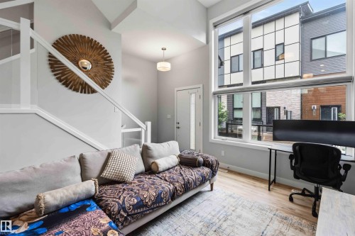 Two-story living area featuring tall windows with roller shades, wood-finish flooring, and a white staircase with a glass panel railing - 33 1729 Keene Crescent, Edmonton, AB 