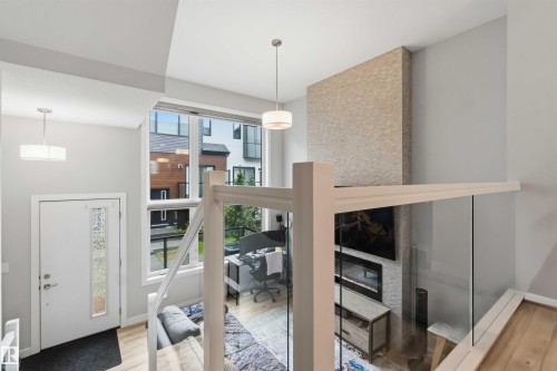 Two-story living space featuring an electric fireplace with a textured stone surround, large windows, wood-finish flooring, and a glass-paneled railing system - 33 1729 Keene Crescent, Edmonton, AB 