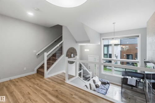 Open-concept living area featuring wood-finish flooring and a contemporary glass and white wood railing - 33 1729 Keene Crescent, Edmonton, AB 