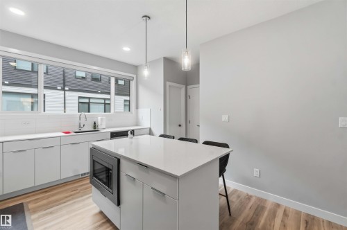 Modern kitchen featuring a central island with integrated microwave, pendant lighting, and wood-finish flooring - 33 1729 Keene Crescent, Edmonton, AB 