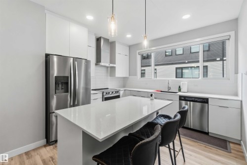 Modern kitchen featuring white flat-panel cabinetry, stainless steel appliances, a white subway tile backsplash, and a large central island with a light-toned countertop - 33 1729 Keene Crescent, Edmonton, AB 