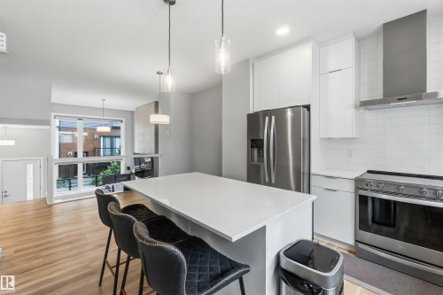 Modern kitchen featuring a white countertop island, stainless steel appliances, white cabinetry, and a tile backsplash - 33 1729 Keene Crescent, Edmonton, AB 