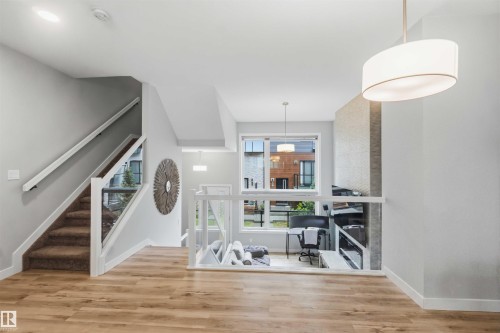 Multi-level interior featuring wood-finish flooring, a carpeted staircase with glass panel railing, and recessed lighting - 33 1729 Keene Crescent, Edmonton, AB 