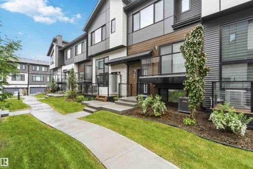Modern multi-level townhome featuring a mixed-material exterior, black-framed windows, and glass panel balconies - 33 1729 Keene Crescent, Edmonton, AB 