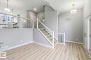 Open-concept main level featuring light wood-finish flooring, a glass and white railing system, recessed lighting, and a modern two-panel entry door with matte black hardware - 33 1729 Keene Crescent, Edmonton, AB 