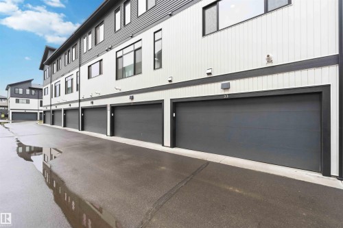 Exterior facade featuring vertical and horizontal siding, multiple dark grey garage doors, exterior wall sconces, and dark-framed windows - 33 1729 Keene Crescent, Edmonton, AB 
