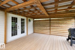 Covered outdoor patio featuring light wood-finish decking, a slatted wood privacy screen, and a corrugated metal roof supported by exposed wood beams - 