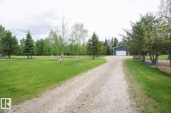 Gravel driveway leading to a detached blue outbuilding with a white garage door - 