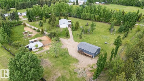 Expansive property featuring a main residence with a white exterior and a dark roof, a detached gray outbuilding with a dark roof, additional smaller white outbuildings, a gravel driveway, and abundant surrounding greenery - 209 5128 Highway 18, Rural Barrhead County, AB 