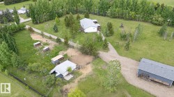 Expansive property featuring multiple outbuildings, a main residence with a gray shingle roof, and a gravel driveway - 