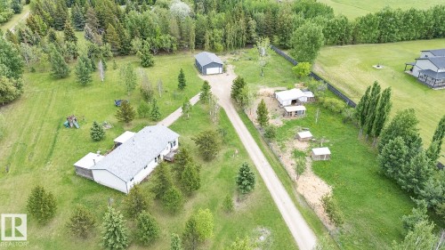 Expansive property featuring a single-story residence with a gray shingle roof, a detached garage, a gravel driveway, mature trees, and outbuildings - 209 5128 Highway 18, Rural Barrhead County, AB 