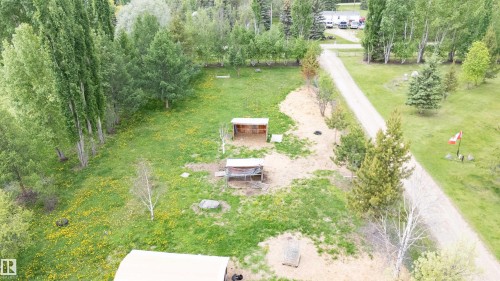 Expansive green space featuring a gravel driveway, mature trees, two outbuildings, and a flagpole - 209 5128 Highway 18, Rural Barrhead County, AB 