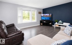 Living area featuring wood-finish flooring, a bay window with a bright exterior outlook, a dark accent wall, and light gray wall finishes - 