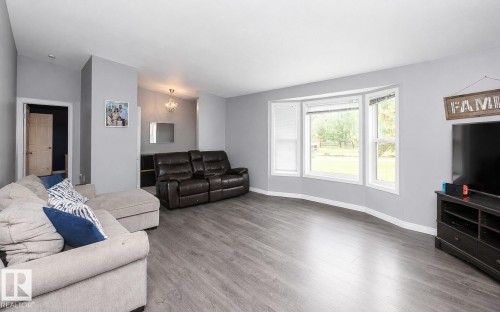 Spacious living area featuring wood-finish flooring, light gray walls, and a prominent bay window - 209 5128 Highway 18, Rural Barrhead County, AB 