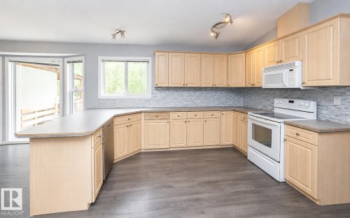 Kitchen featuring light wood cabinetry, a tiled backsplash, laminate countertops, and stainless steel appliances - 209 5128 Highway 18, Rural Barrhead County, AB 