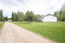 Expansive green lawn surrounds a white-sided residence with a dark gray roof - 209 5128 Highway 18, Rural Barrhead County, AB 
