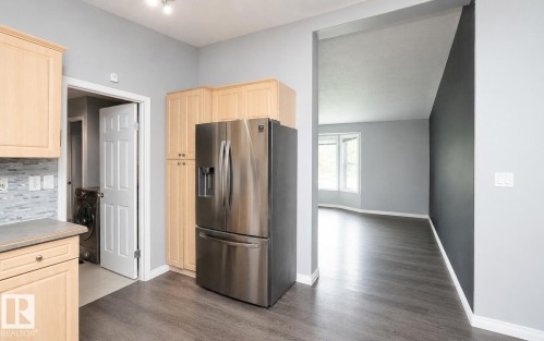 Kitchen featuring light wood-finish cabinetry, stainless steel refrigerator, and tiled backsplash - 209 5128 Highway 18, Rural Barrhead County, AB 