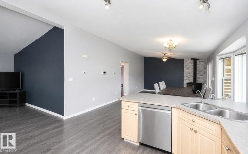 Open-concept living space featuring wood-finish flooring, a kitchen island with a double basin sink, stainless steel dishwasher, and light wood cabinetry - 209 5128 Highway 18, Rural Barrhead County, AB 