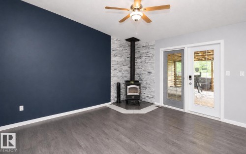 Interior space featuring wood-finish flooring, a corner wood-burning stove with a stacked stone surround, and double glass-paneled doors - 209 5128 Highway 18, Rural Barrhead County, AB 