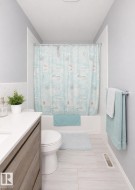Bathroom featuring a built-in tub with tile surround, wood-finish vanity with an integrated sink, white countertop, and light-toned tile flooring - 
