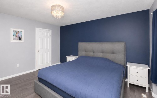 Bedroom featuring an accent wall, gray walls, wood-finish flooring, and a crystal chandelier - 209 5128 Highway 18, Rural Barrhead County, AB 
