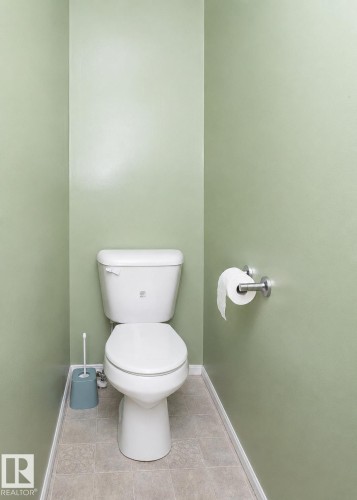 Powder room featuring a white two-piece toilet, ceramic tile flooring, a chrome toilet paper holder, and light green wall paint - 209 5128 Highway 18, Rural Barrhead County, AB 