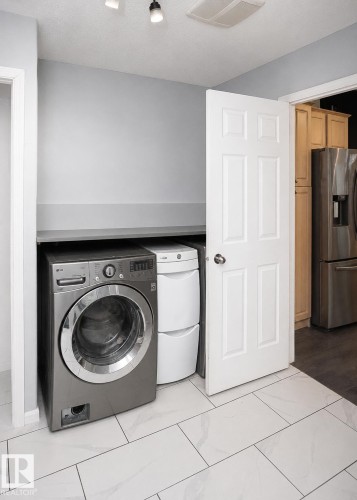 Dedicated laundry area featuring a front-load washer, stacked dryer unit, and overhead shelving - 209 5128 Highway 18, Rural Barrhead County, AB 