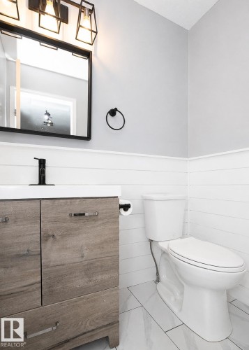Modern bathroom featuring a wood-finish vanity with integrated white sink, black wall-mounted faucet, and black framed mirror - 209 5128 Highway 18, Rural Barrhead County, AB 