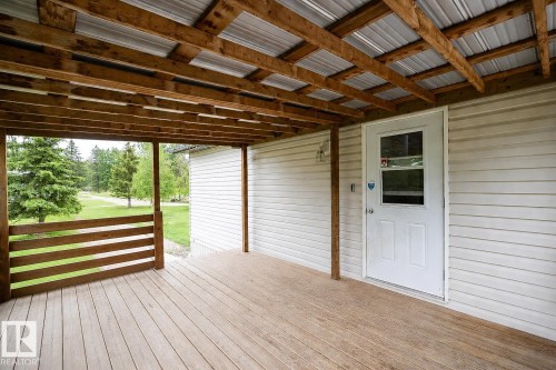 Covered porch with wood-finish decking, exposed wood beam ceiling, metal roof, and white vinyl siding - 209 5128 Highway 18, Rural Barrhead County, AB 