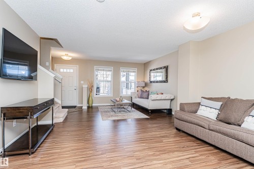 Open concept living area featuring wood-finish flooring, neutral wall tones, and multiple windows - 31 4029 Orchards Drive, Edmonton, AB 