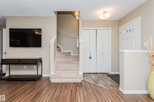 Entryway featuring wood-finish flooring, a carpeted staircase with white railings, and a front door with decorative glass inserts - 31 4029 Orchards Drive, Edmonton, AB 