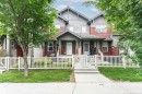 Multi-level townhouse exterior featuring vertical and horizontal siding, a fenced front yard with grass, mature trees, a concrete walkway, and a covered porch entry - 31 4029 Orchards Drive, Edmonton, AB 