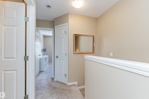 Carpeted hallway featuring warm neutral wall tones and white trim - 31 4029 Orchards Drive, Edmonton, AB 