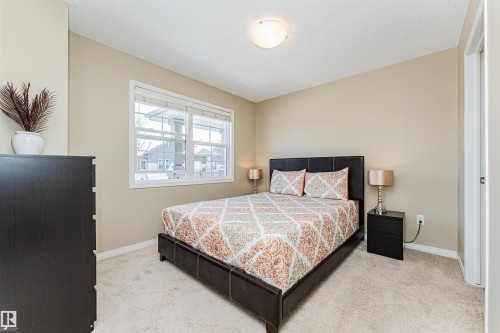 Carpeted bedroom featuring a large window, neutral wall tones, and a ceiling-mounted light fixture - 31 4029 Orchards Drive, Edmonton, AB 