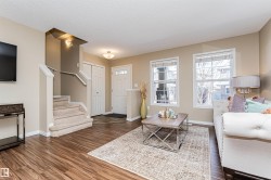 Open concept living space featuring wood-finish flooring, two large windows, a carpeted staircase with white railings, and a front entry door with transom windows - 