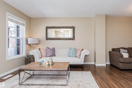 Bright living space featuring a large window, warm wall color, wood-finish flooring, and white baseboards - 31 4029 Orchards Drive, Edmonton, AB 