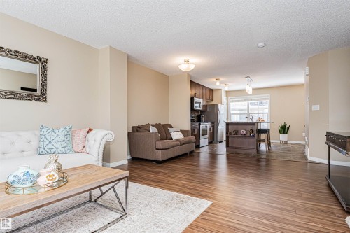 Open-concept living space featuring wood-finish flooring, a kitchen island with seating, stainless steel appliances, and ceiling-mounted light fixtures - 31 4029 Orchards Drive, Edmonton, AB 